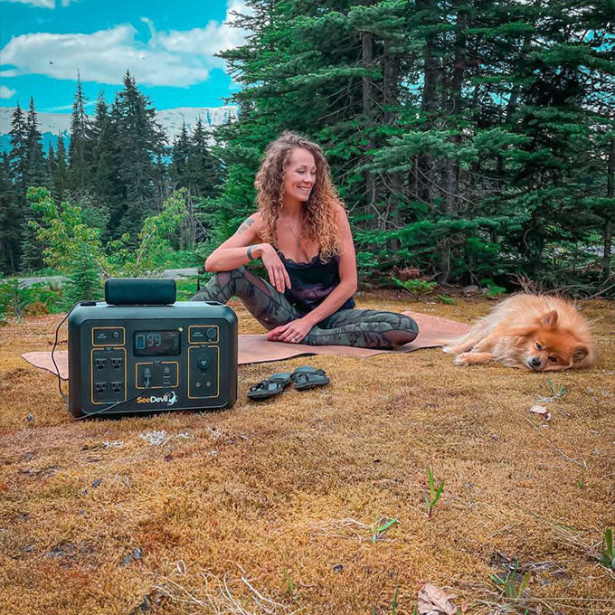 Image showing a woman using the portable power station to charge a speaker in nature