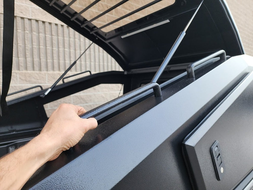 A Person Holding Onto The Integrated Grab Handles On The GAIA Campers  Gladiator Shadow Top Truck Cap