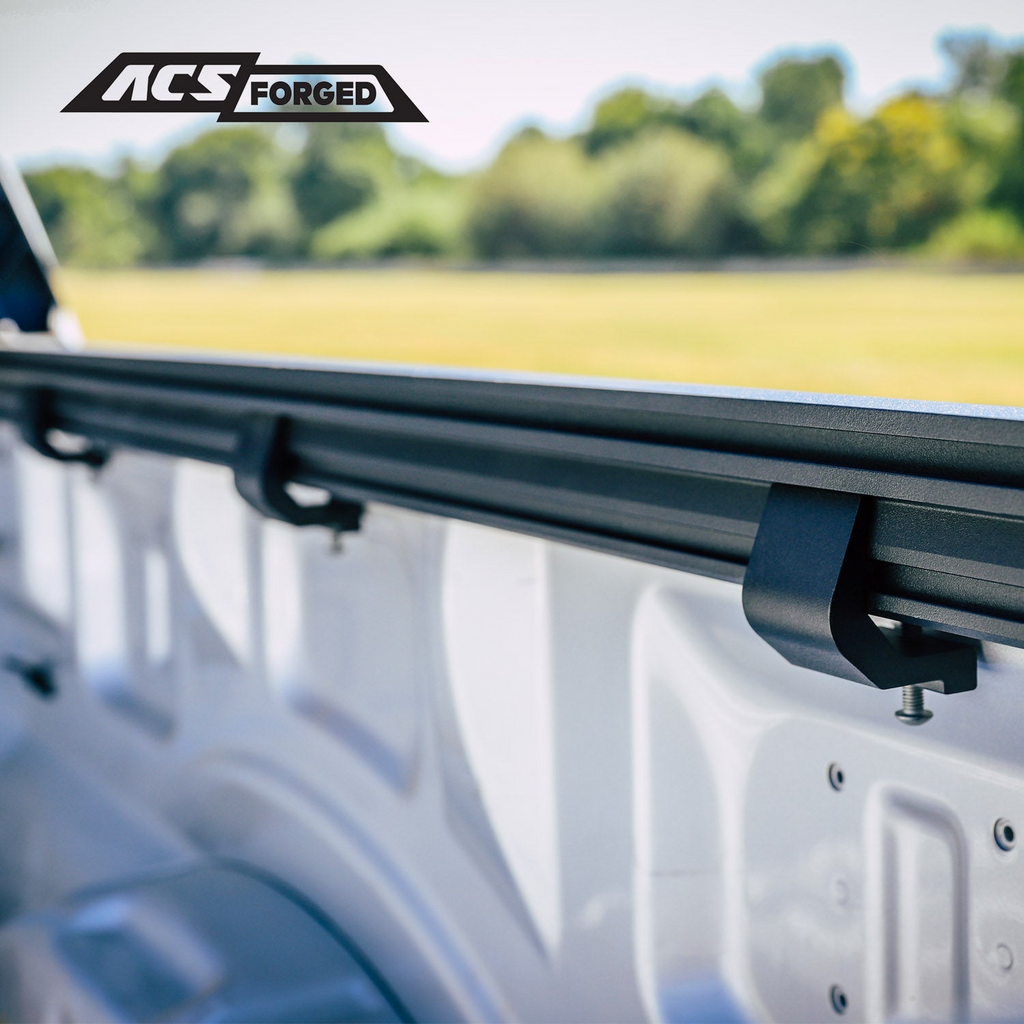 Wide-angle view inside a white truck bed showing multiple black C-clamps installed along the length of the ACS Forged mounting rail.