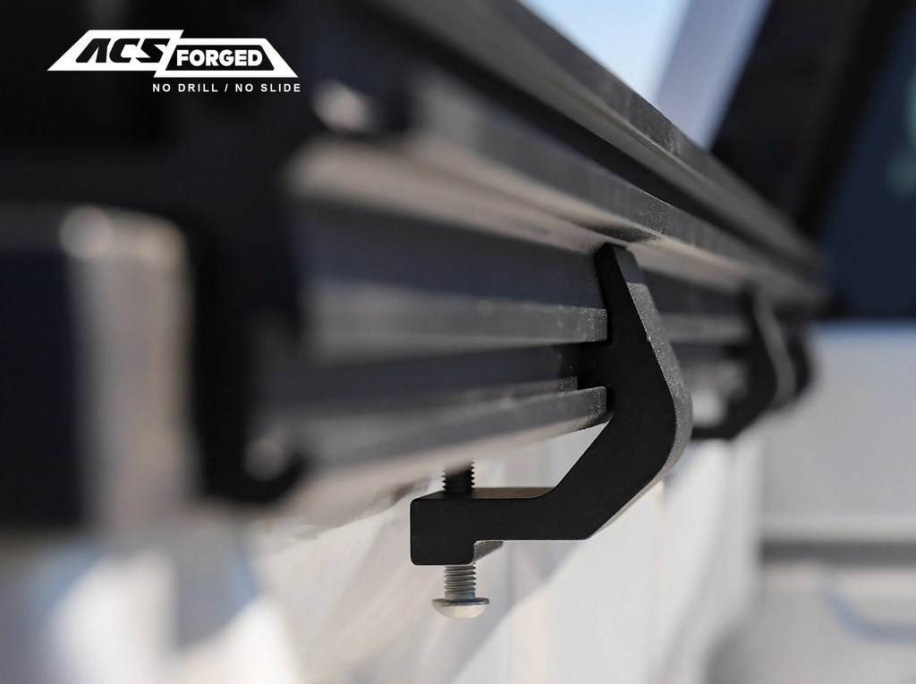 A detailed low-angle shot showing the underside of the "no-drill" mounting clamps and the T-slot channel of the ACS Forged bed rail.
