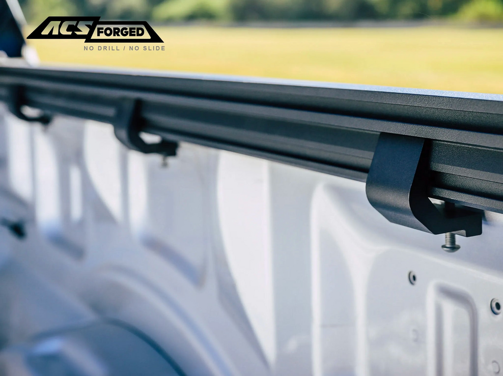 A close-up view of the Leitner ACS Forged "no-drill" mounting clamps secured to the inner bed rail of a white Chevrolet truck.