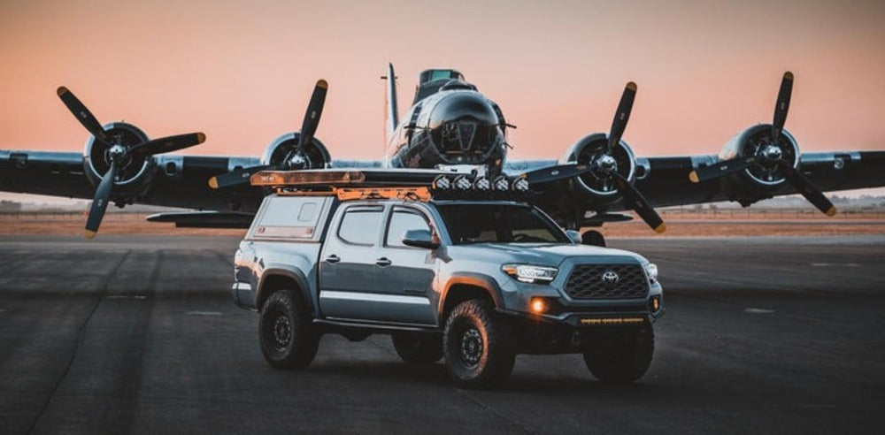 upTOP Overland Alpha Tacoma Roof Rack Mounted On A Toyota Tacoma With A Plane Behind It