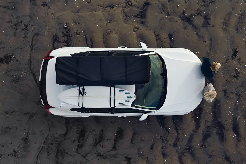 Packed Thule 2-Person Roof Top Tent next To A surf Board On A Vehicles Roof Rack