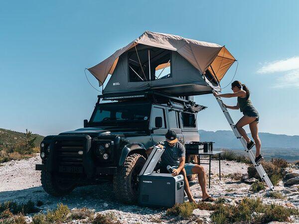 People Sitting And Climbing Into The Front Runner Roof Top Tent That Is Mounted On A Vehicle