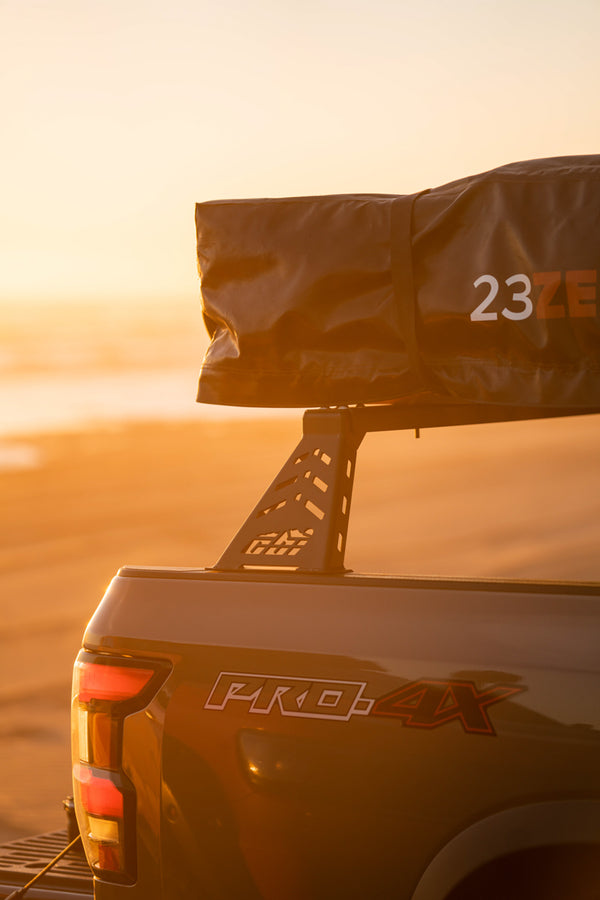 3rd gen nissan frontier with mounted CBI bed bars with a sunset behind it
